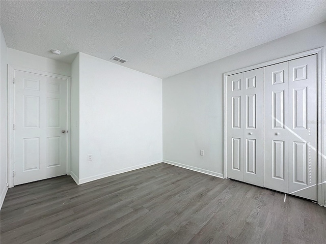 unfurnished bedroom with a textured ceiling, dark wood-type flooring, and a closet