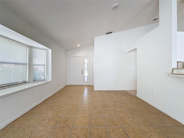 tiled empty room featuring a textured ceiling and vaulted ceiling