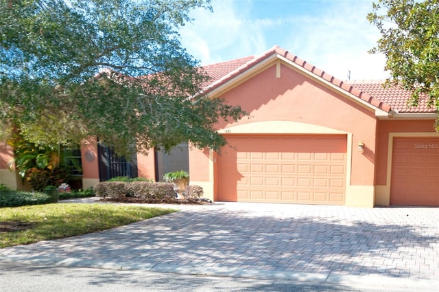 mediterranean / spanish-style house featuring an attached garage, a tile roof, decorative driveway, and stucco siding