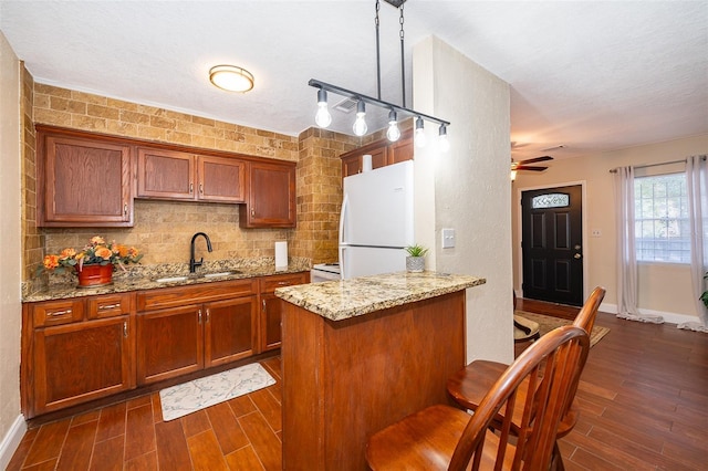 kitchen with pendant lighting, white refrigerator, sink, ceiling fan, and light stone counters