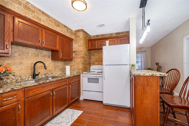 kitchen featuring white appliances, light stone counters, a breakfast bar area, and sink