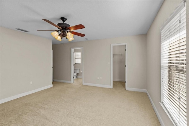 unfurnished bedroom featuring light carpet, a walk in closet, ceiling fan, connected bathroom, and a closet