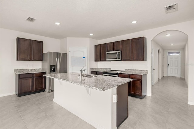 kitchen with sink, a breakfast bar area, a kitchen island with sink, dark brown cabinets, and appliances with stainless steel finishes