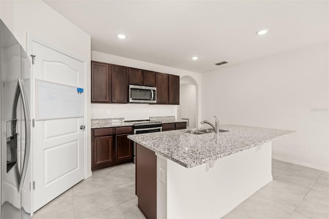 kitchen with a kitchen bar, a kitchen island with sink, sink, appliances with stainless steel finishes, and light stone counters