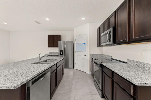 kitchen featuring sink, light tile patterned floors, stainless steel appliances, and an island with sink