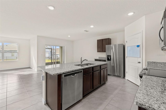 kitchen with dark brown cabinets, stainless steel appliances, a center island with sink, and sink