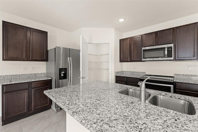 kitchen featuring dark brown cabinets, stainless steel appliances, light stone counters, and light tile patterned flooring