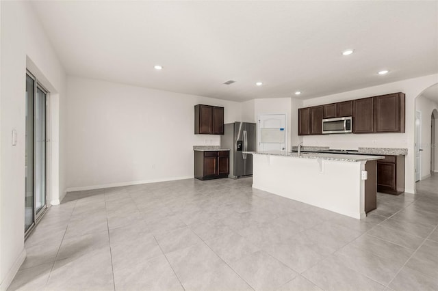 kitchen featuring sink, a kitchen bar, a center island with sink, dark brown cabinets, and appliances with stainless steel finishes