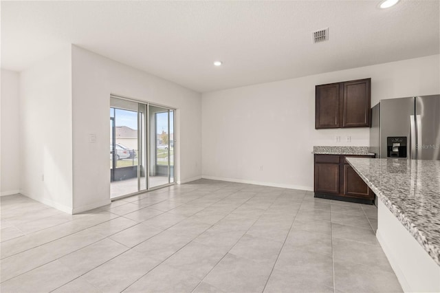 kitchen featuring light stone countertops, stainless steel fridge, dark brown cabinetry, and light tile patterned floors