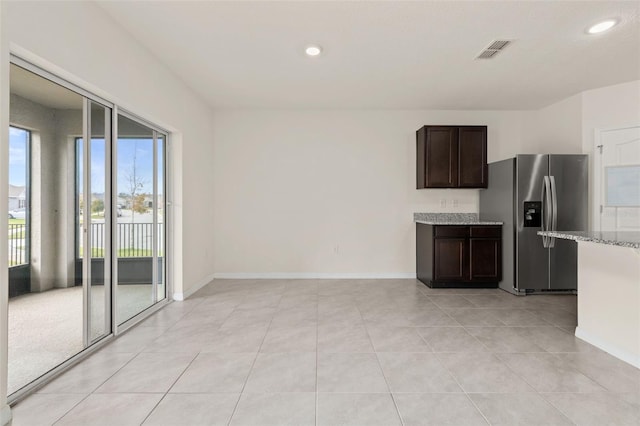 kitchen featuring stainless steel fridge with ice dispenser, dark brown cabinets, light tile patterned floors, and light stone countertops