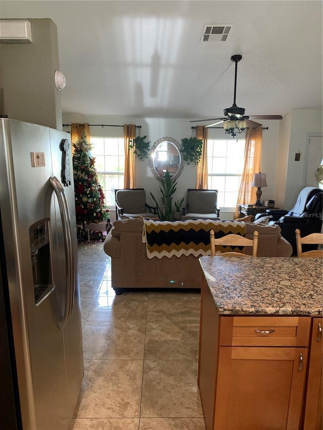 kitchen with stainless steel refrigerator with ice dispenser, stone countertops, light tile patterned floors, and ceiling fan