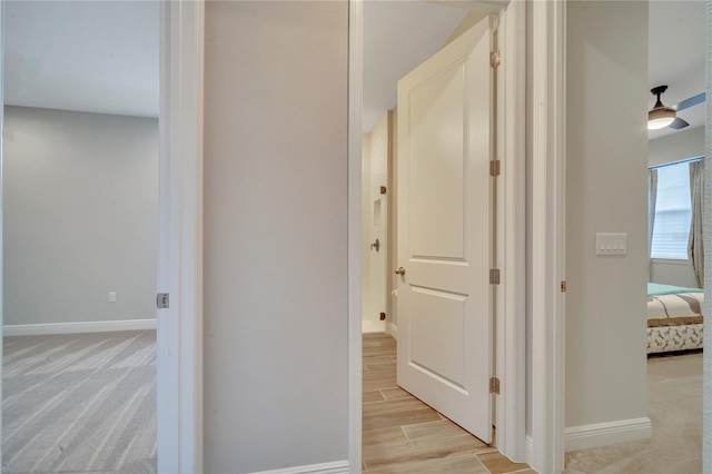 corridor with light wood-type flooring, light carpet, and baseboards