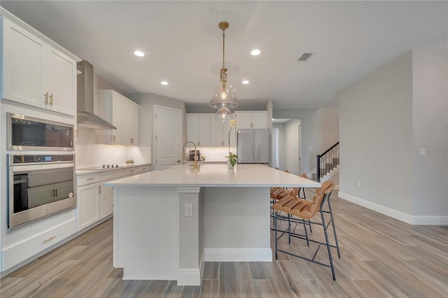 kitchen featuring visible vents, appliances with stainless steel finishes, light wood-style floors, white cabinetry, and wall chimney exhaust hood