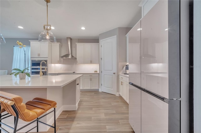 kitchen with light countertops, white cabinetry, light wood finished floors, and wall chimney exhaust hood