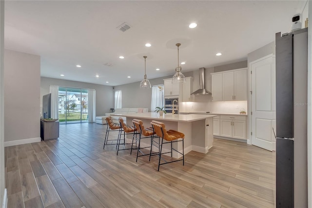 kitchen featuring white cabinetry, wall chimney range hood, light wood-type flooring, freestanding refrigerator, and stainless steel microwave