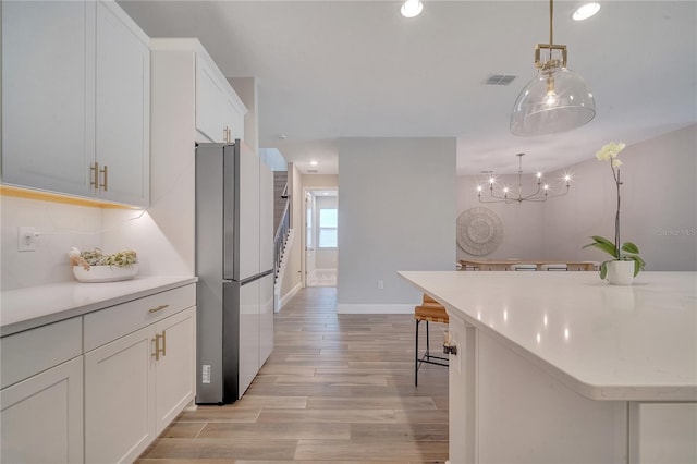 kitchen with light countertops, freestanding refrigerator, visible vents, and white cabinetry