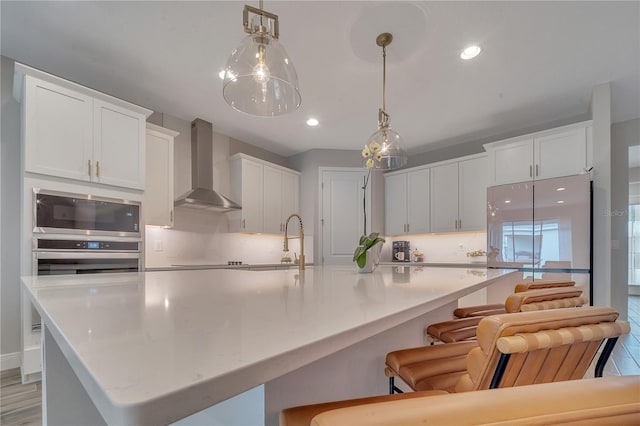 kitchen featuring a sink, white cabinetry, wall chimney range hood, appliances with stainless steel finishes, and backsplash