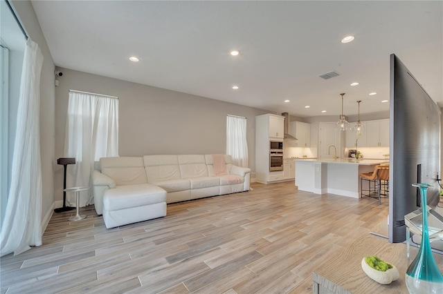 living area featuring baseboards, recessed lighting, visible vents, and light wood-style floors