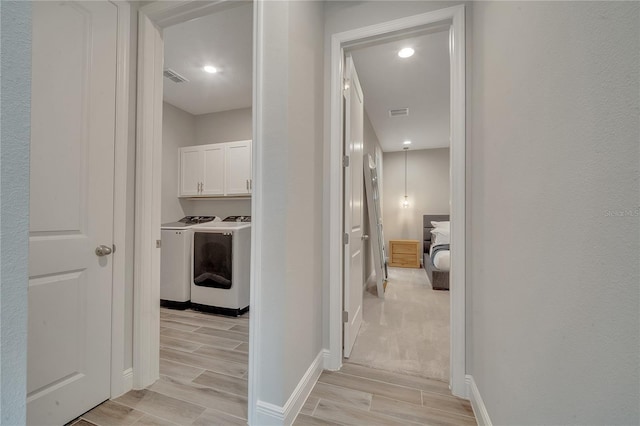 hallway with washing machine and dryer, wood tiled floor, visible vents, and baseboards