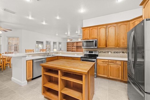 kitchen featuring a center island, wooden counters, sink, ceiling fan, and stainless steel appliances