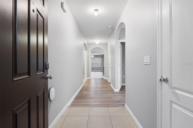 hallway with a textured ceiling and light tile patterned flooring