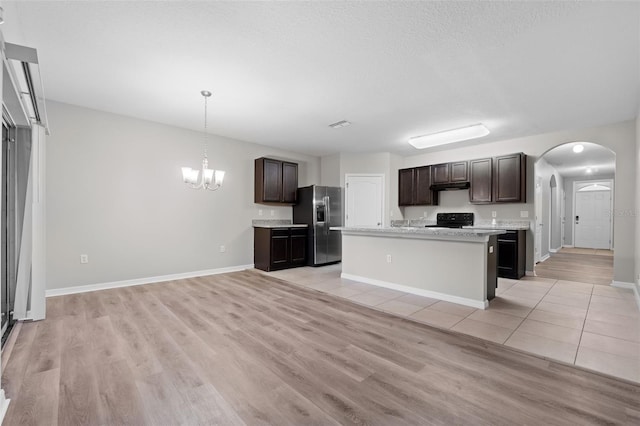 kitchen with black range oven, dark brown cabinets, a kitchen island with sink, decorative light fixtures, and stainless steel fridge with ice dispenser