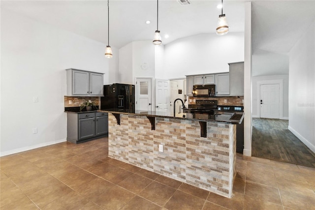 kitchen featuring a breakfast bar, an island with sink, lofted ceiling, hanging light fixtures, and black appliances