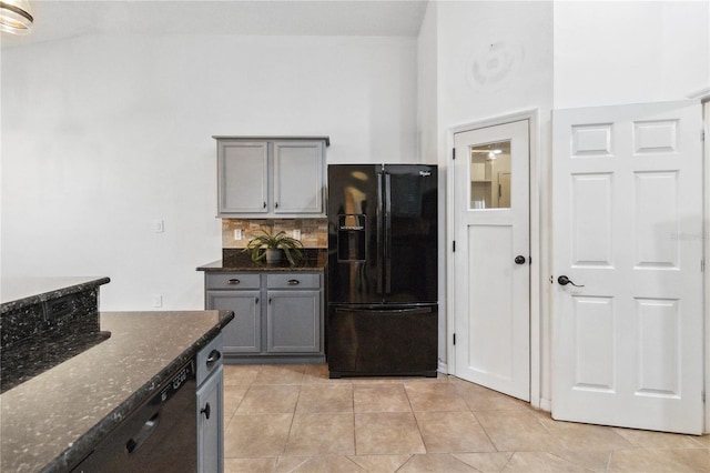 kitchen with gray cabinetry, black fridge, tasteful backsplash, light tile patterned floors, and dark stone counters