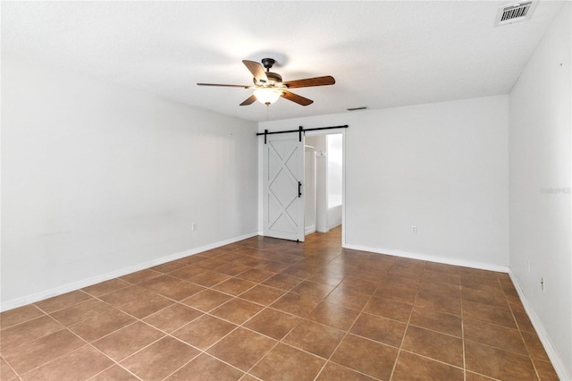 spare room with dark tile patterned floors, a textured ceiling, a barn door, and ceiling fan