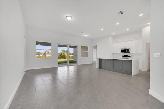 kitchen with white cabinetry, sink, stainless steel appliances, an island with sink, and light tile patterned flooring