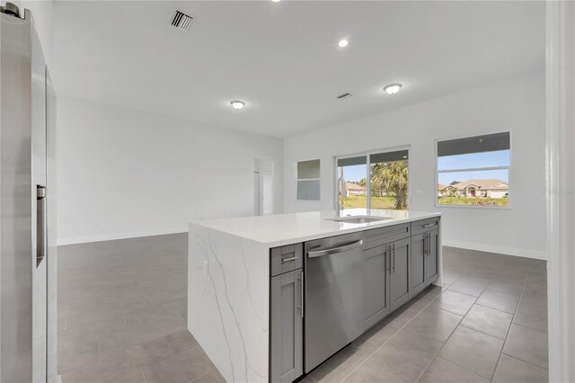 kitchen featuring sink, an island with sink, gray cabinets, light tile patterned flooring, and appliances with stainless steel finishes