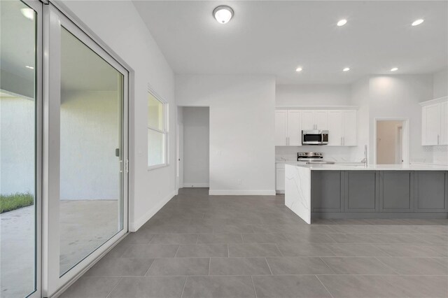 kitchen with kitchen peninsula, appliances with stainless steel finishes, light tile patterned floors, and white cabinetry