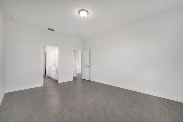 unfurnished bedroom with ensuite bathroom and dark tile patterned floors