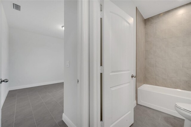 bathroom featuring tile patterned flooring, tiled shower / bath combo, and toilet