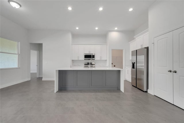 kitchen featuring white cabinets, light tile patterned flooring, a kitchen island with sink, and appliances with stainless steel finishes