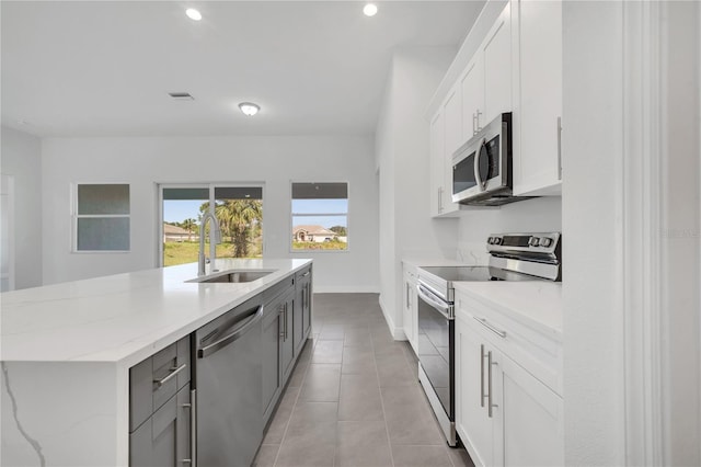 kitchen featuring light stone counters, stainless steel appliances, a kitchen island with sink, sink, and white cabinets