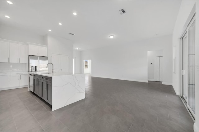 kitchen featuring stainless steel refrigerator with ice dispenser, light stone counters, a kitchen island with sink, sink, and white cabinets