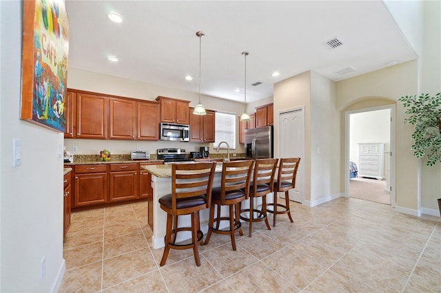 kitchen with hanging light fixtures, light stone counters, a breakfast bar area, a kitchen island with sink, and appliances with stainless steel finishes