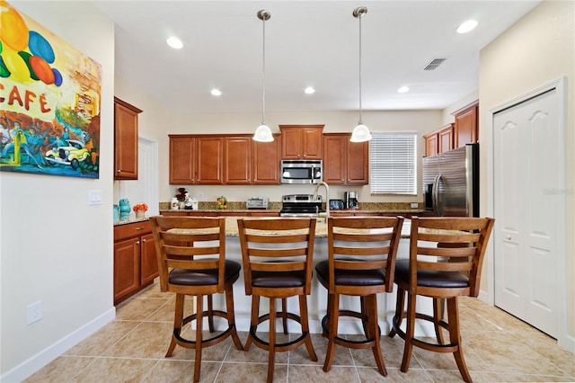 kitchen with a center island with sink, light tile patterned floors, appliances with stainless steel finishes, decorative light fixtures, and a kitchen bar