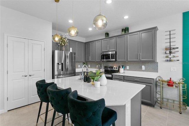 kitchen with pendant lighting, gray cabinetry, a kitchen bar, a kitchen island with sink, and stainless steel appliances