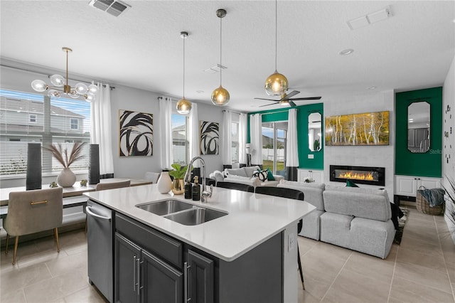 kitchen with decorative light fixtures, sink, a textured ceiling, and an island with sink