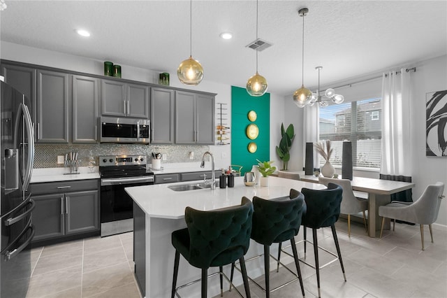 kitchen with decorative light fixtures, sink, gray cabinets, a kitchen bar, and stainless steel appliances