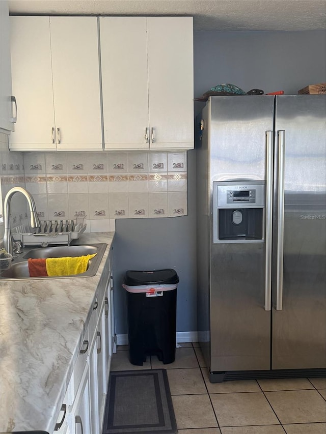 kitchen with white cabinets, sink, stainless steel refrigerator with ice dispenser, decorative backsplash, and light tile patterned flooring