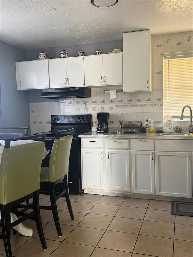 kitchen featuring black electric range oven, sink, white cabinets, and light tile patterned floors