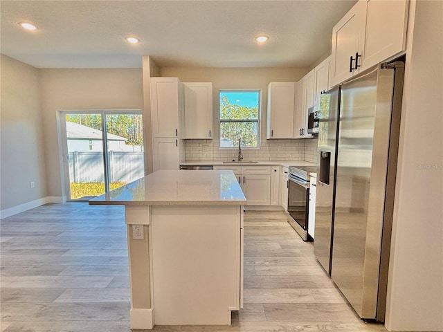 kitchen with sink, a kitchen island, light stone counters, white cabinetry, and stainless steel appliances