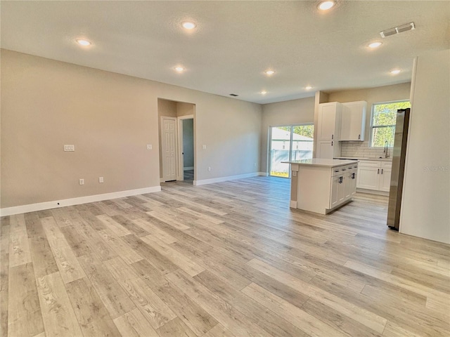 kitchen with stainless steel refrigerator, white cabinetry, light hardwood / wood-style floors, decorative backsplash, and a kitchen island