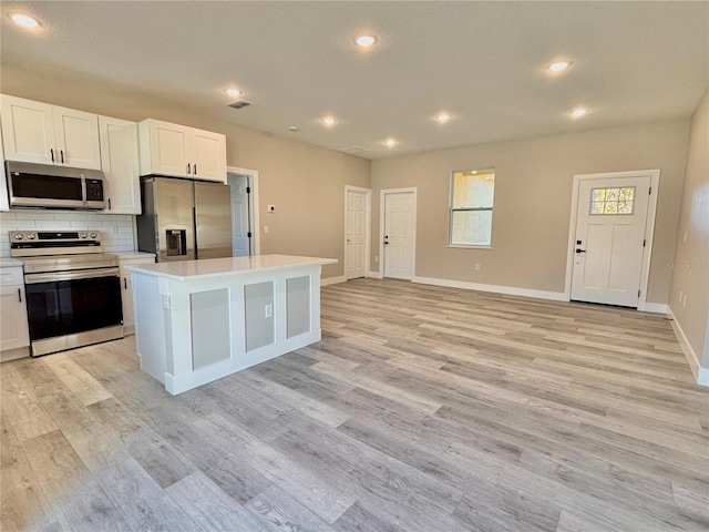 kitchen with stainless steel appliances, a kitchen island, light hardwood / wood-style flooring, backsplash, and white cabinets