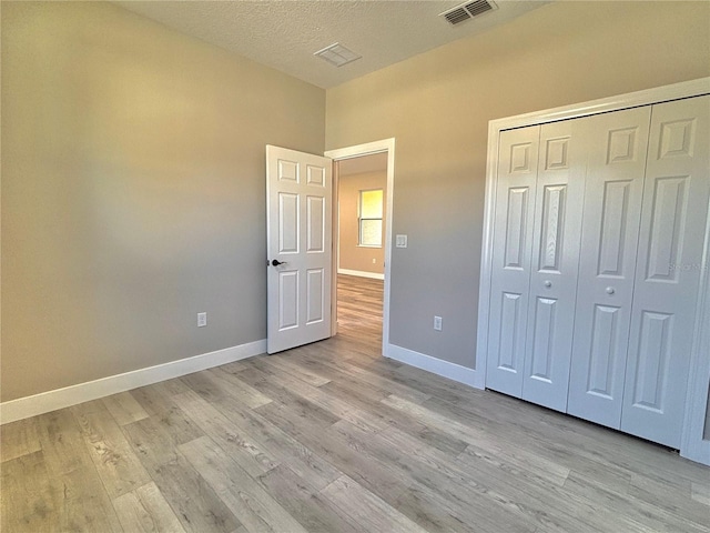 unfurnished bedroom featuring a closet, a textured ceiling, and light hardwood / wood-style flooring