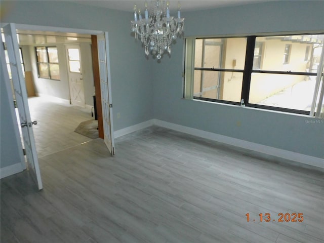 empty room featuring a notable chandelier and light wood-type flooring