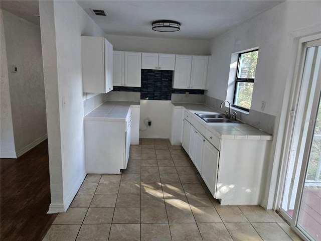 kitchen featuring tasteful backsplash, sink, white cabinets, and light tile patterned floors